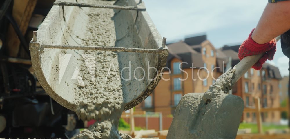 Building a cottage. Workers take concrete from a mixer into a wooden formwork