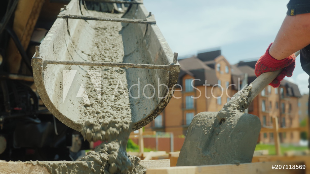 Building a cottage. Workers take concrete from a mixer into a wooden formwork
